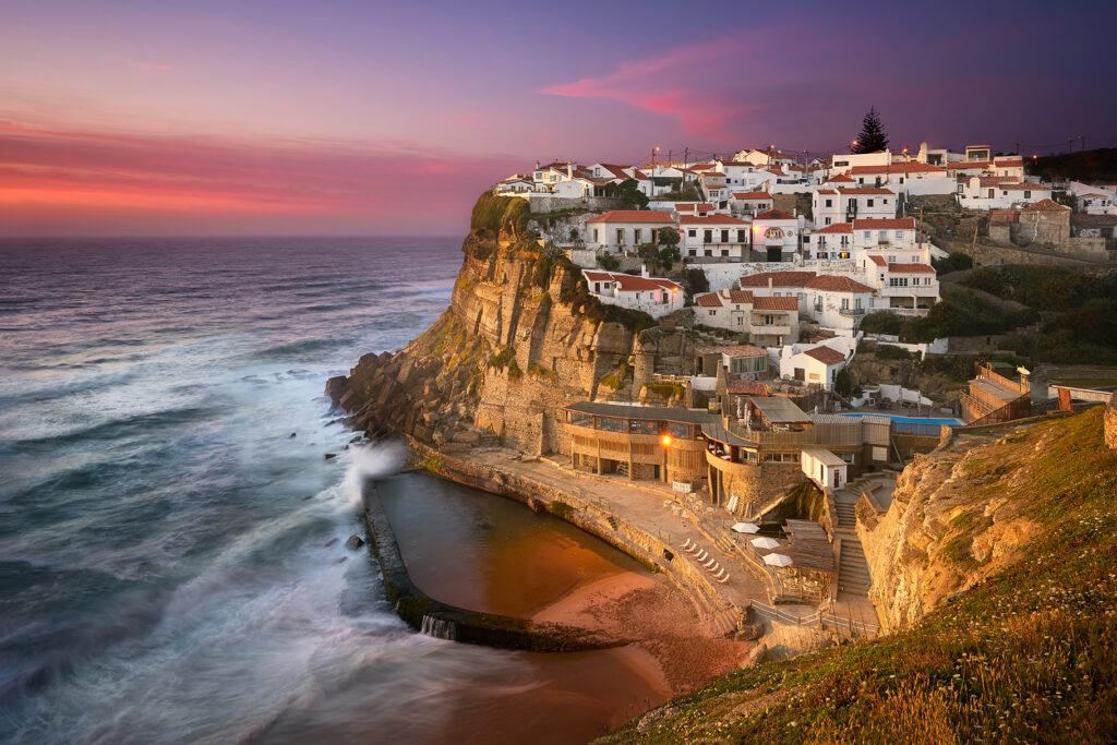 A beautiful village on a cliff over the ocean underneath the colorful sky